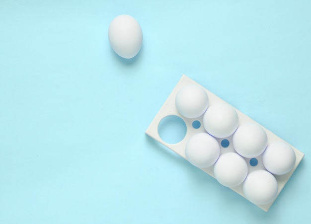 Plastic tray with white eggs on blue pastel background, minimalism trend, top view