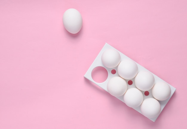 Plastic tray with white eggs on a pink pastel background