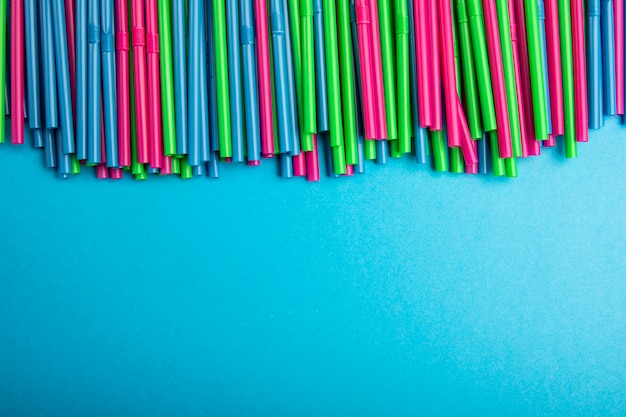 Plastic tubes concept. Multi Colored cocktail straws lying on a blue background 