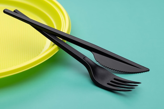 Фото Пластиковая посуда крупным планом. одноразовая желтая тарелка, черные столовые приборы на ярко-зеленом фоне.