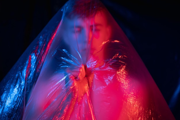 Plastic vervuiling. Intreepupil portret. Red de natuur. Ecologie probleem. Moe geïsoleerde shirtloze man met gesloten ogen vouwen in de hand polyethyleenfilm in roze blauw neonlicht op donker onscherp.