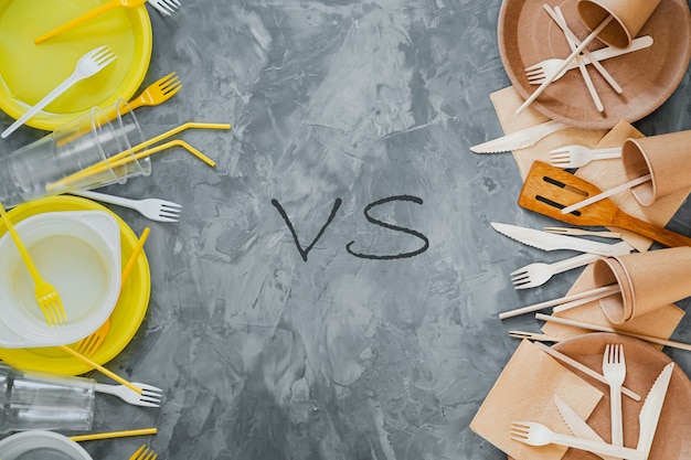 Plastic vs sustainable dinnerware choice concept. top above  view photo of white and yellow plastic and wooden  utensils compared on grey background.