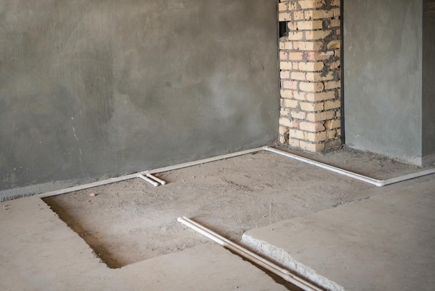 Пластиковые водопроводные трубы на полу и оштукатуренные стены в новом доме первичный ремонт в комнате