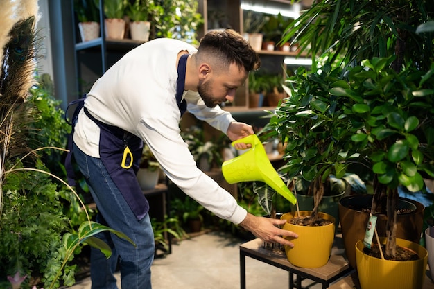 A plastic watering can florist pours water on a potted plant in a shop