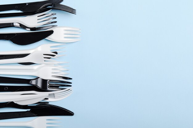 Plastic white and black disposable forks and knives on a blue background. Plastic dishes. Copy space, top view, flat lay.