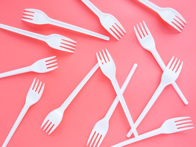 Plastic white forks are scattered on a pink background