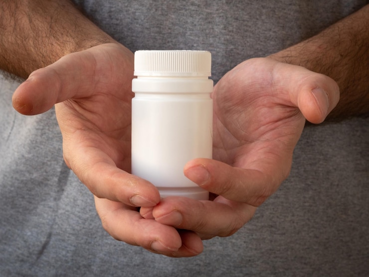男性の手で薬の丸薬とプラスチック製の白い瓶