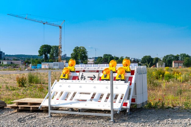 Plastic white and red barrier boards with orange warning lights stacked in front of a construction site