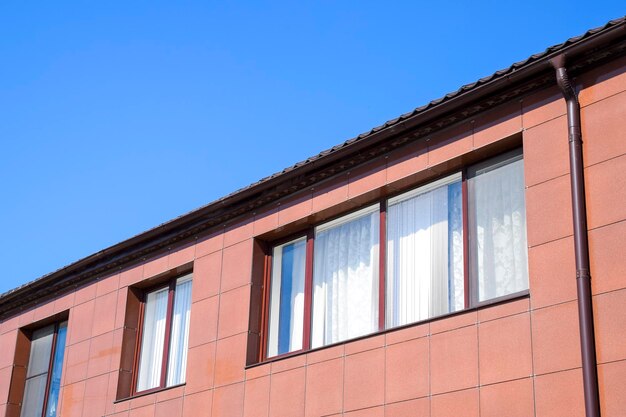 Plastic windows on the house and a spillway system on the roof House with plastic windows and a brown roof of corrugated sheet