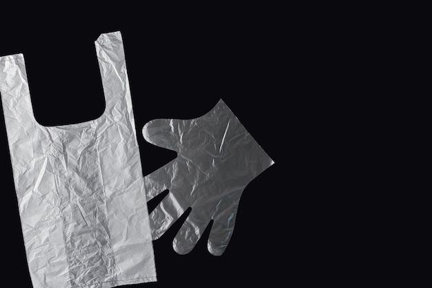Plastic zak met handvatten handschoenen op een zwarte achtergrond Gebruikte plastic zak voor recycling Concept ecologie planeetvervuiling met plastic cellofaan polyethyleen