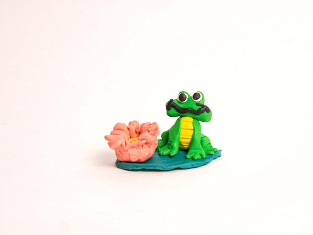 Plasticine craft green frog on a leaf of a water lily with a flower