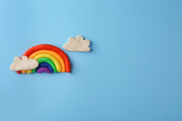 Plasticine rainbow with clouds on color background