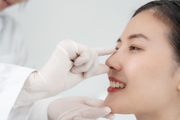 Plastische chirurgie schoonheid Aziatische glimlach en gelukkig na de operatie chirurgische ingrepen die de vorm van de neus veranderen arts onderzoekt de neus van de patiënt voor de neusplastiek medische hulp gezondheid