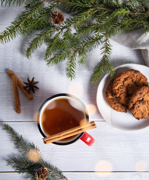 Plat kerstthee met kaneel en kruiden in een rode mok met zelfgemaakte koekjes op een houten ondergrond met een kerstboom en een bokeh. Bovenaanzicht