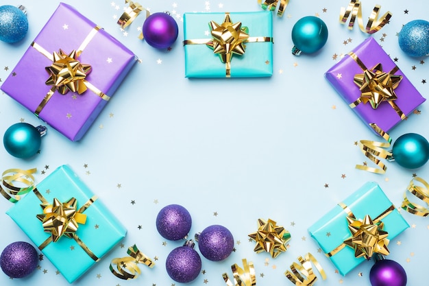 Plat lag achtergrond voor feest Kerstmis en Nieuwjaar. Geschenkdozen zijn paars en turquoise met gouden linten strikken en confetti sterren op een blauwe achtergrond. bovenaanzicht kopie ruimte.