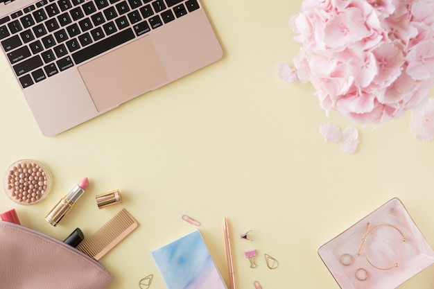 Plat lag en bovenaanzicht van kantoor aan huis vrouw bureau. Vrouwelijke werkruimte met laptop, hortensia bloemen, schoonheid accessoires, blauwe agenda op pastel gele achtergrond.