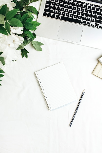 Plat lag kantoor aan huis Bureau met laptop, notebook, witte pioenrozen bloemen boeket op wit oppervlak