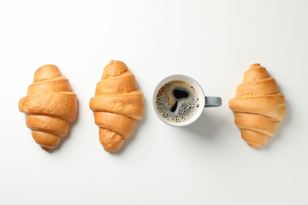 Plat lag met croissants en kopje koffie op witte achtergrond, bovenaanzicht