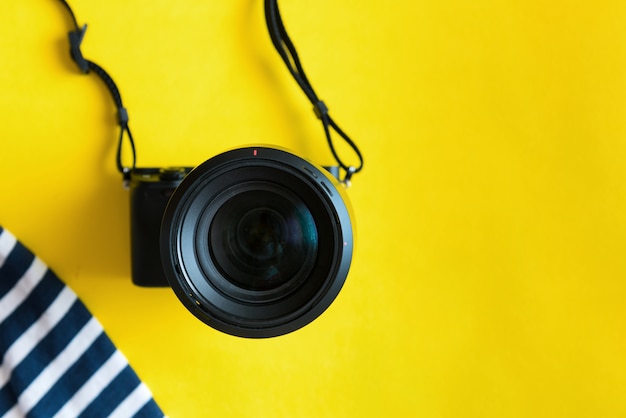 Plat lag reizigerstoebehoren op gele achtergrond met blauwe kleding, camera en zonnebril.