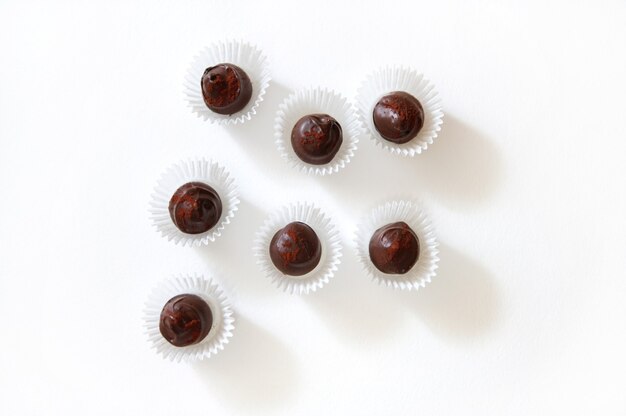 Plat lag samenstelling van chocoladetruffels bestrooid met gevriesdroogde aardbeien in papieren wikkels op een witte ondergrond