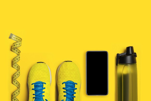 Plat lag shot van sportuitrusting. Sneakers, water, koptelefoon en telefoon op gele achtergrond. Focus ligt alleen op de sneakers