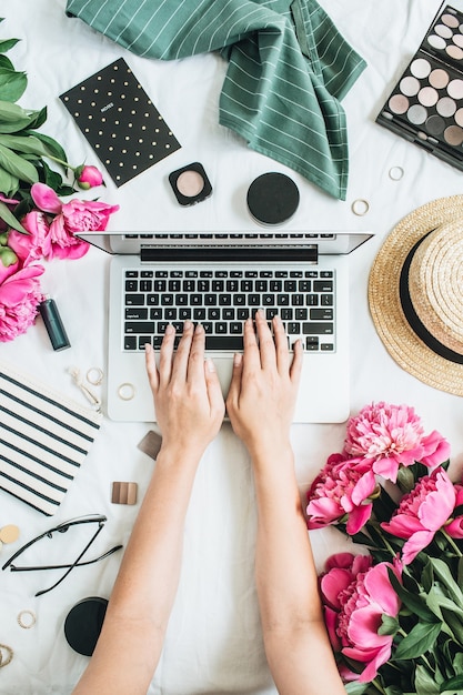 Plat lag stijl bureau met laptop, roze pioenroos bloemen, cosmetica, accessoires