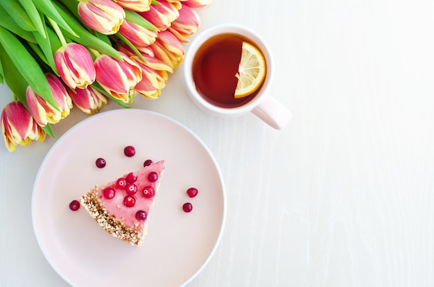 Plat lag voor ontbijt, ochtend met bloemen tulpen, cake, thee in roze mok op witte achtergrond.