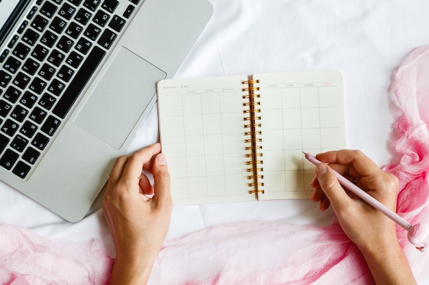 Plat lag werkruimte met laptop, vrouw hand schrijven pen in planner