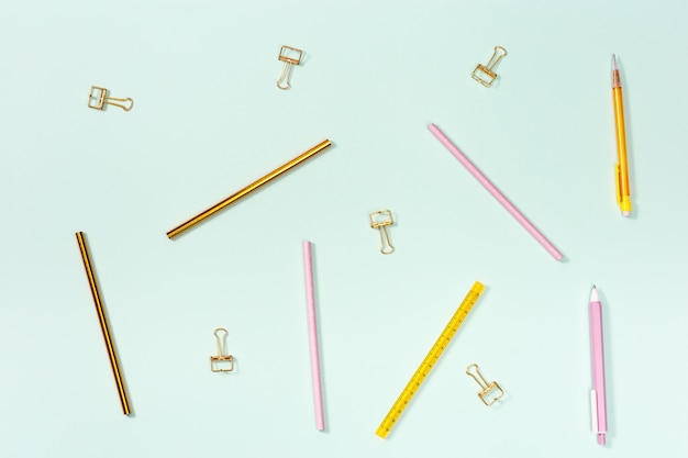 Plat leggen met briefpapier voor school of kantoor. Roze en gouden kleurpotloden, pennen en metalen paperclips.