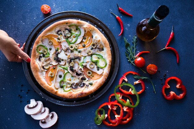 Plat leggen met traditionele Italiaanse pizza met champignons, peper en tomaten op donkerblauwe stenen tafel
