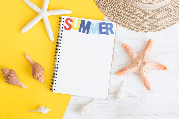 Plat leggen notebook en zeeschelp voor zomervakantie op geel papier op whitewood