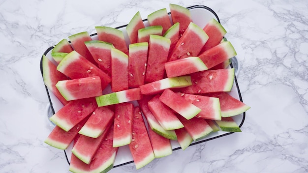Plat leggen. Rode watermeloen in kleine stukjes snijden op een witte snijplank.
