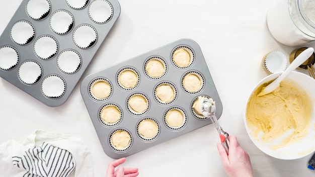 Foto plat leggen. stap voor stap. cupcakebeslag in cupcakevormpjes scheppen om vanillecupcakes te bakken.