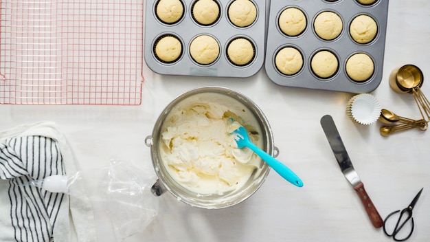 Plat leggen. Stap voor stap. Een witte botercrème frosting in een spuitzak scheppen om vanille cupcakes te versieren.