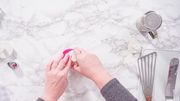 Plat leggen. Stap voor stap. Sneeuwvlokken uitsnijden met koekjes uitstekers uit roze fondant op een marmeren aanrechtblad.