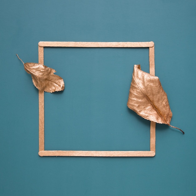 Plat leggen van bladgoud en een frame op een turquoise achtergrond met kopieerruimte. Minimalistisch concept van oogsten, herfst