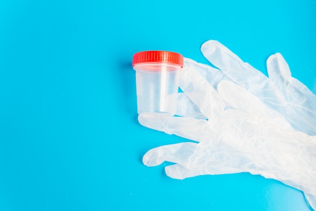 Plat leggen van de medische latex handschoenen en lege plastic test container met kopie ruimte op de blauwe achtergrond