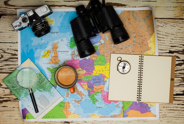 Plat leggen van het reisplanningsconcept. Bovenaanzicht van een dagboek, een verrekijker, een kompas, een retro fotocamera, een koffie en een kaart van Europa op een witte houten tafel