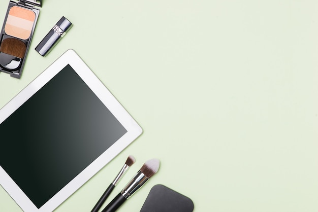 Plat leggen van make-up cosmetische producten met digitale tablet op lichte kleur achtergrond