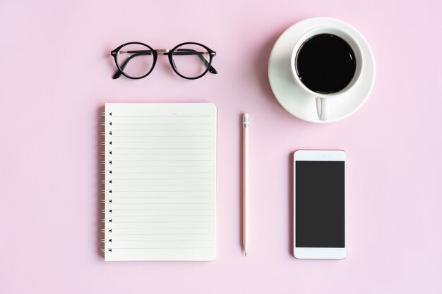 Plat leggen van mobiele telefoon, een kopje koffie, bril en notitieblok van zakenvrouw op roze tafel in kantoor. Business en technologie concept bovenaanzicht en kopieer ruimte.
