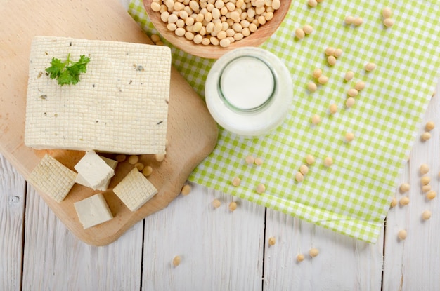 Plat leggen van niet-zuivel-alternatieven sojamelk of yoghurt in glazen fles en tofu op witte houten tafel met sojabonen in kom opzij