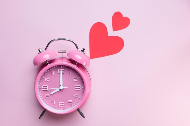 Plat leggen van roze wekker met rood hartpapier Concept van tijd voor liefde, vriendschap en daten van menselijke relaties