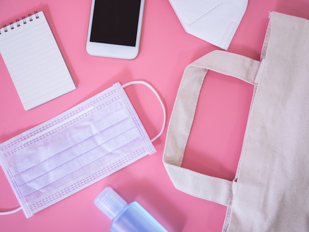Plat leggen van smartphone, chirurgisch masker, creditcard, notebook en alcohol gel ontsmettingsmiddel op roze achtergrond, bovenaanzicht met kopie ruimte voor tekst.