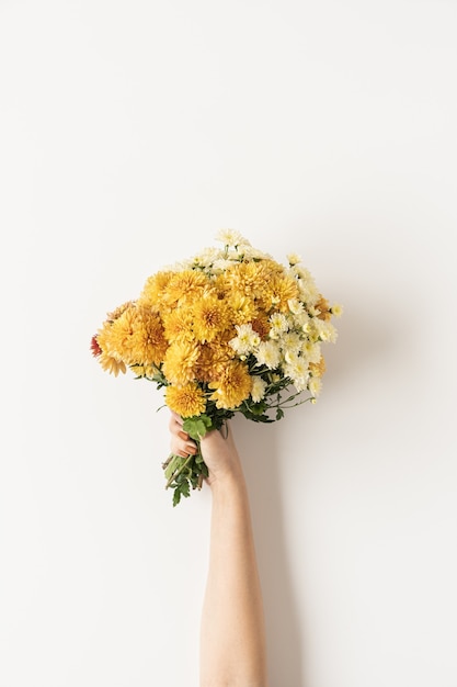 Plat leggen van vrouwelijke hand met gele en gember wilde bloemen boeket vallen op wit. bovenaanzicht