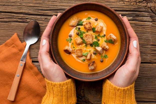 Plat leggen van winterpompoensoep in kom vastgehouden door handen met lepel en croutons