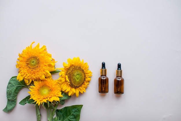 Foto plat leggen van zonnebloemen en flessen voor cosmetisch serum of crème op een lichtroze achtergrond