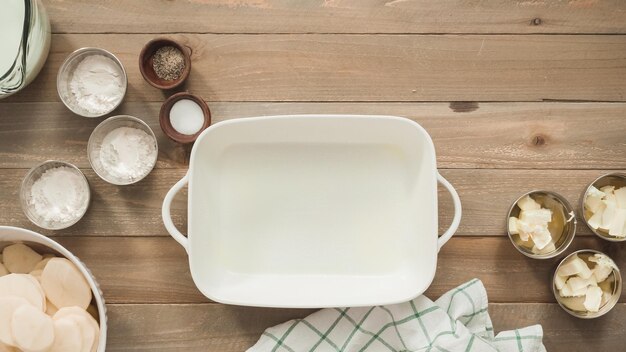 Plat leggen. Voorbereiding van geschulpte aardappelen in een witte keramische ovenschaal.