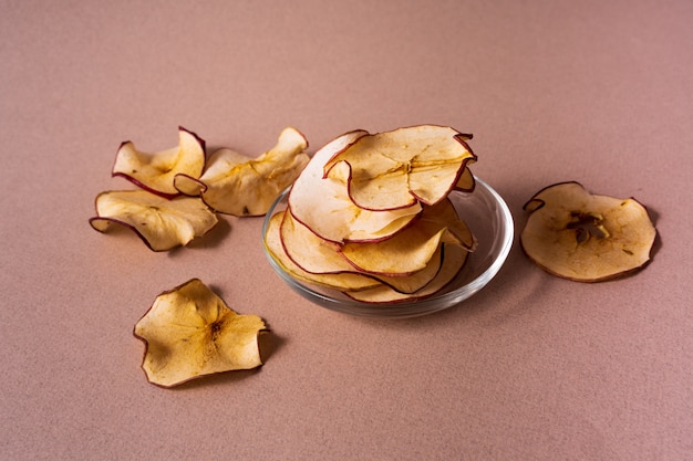 Plat van gedroogde appels chips in een glazen pot over roze achtergrond.