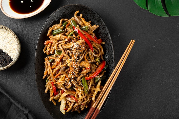 Foto piatto di spaghetti di soba di grano saraceno asiatico con verdure, funghi e pollo su sfondo scuro