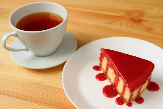 Plate of baked cheesecake with raspberry sauce with a cup of hot tea served on wooden table